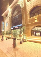 A hotel entrance with a large sign, arched windows, and potted plants.