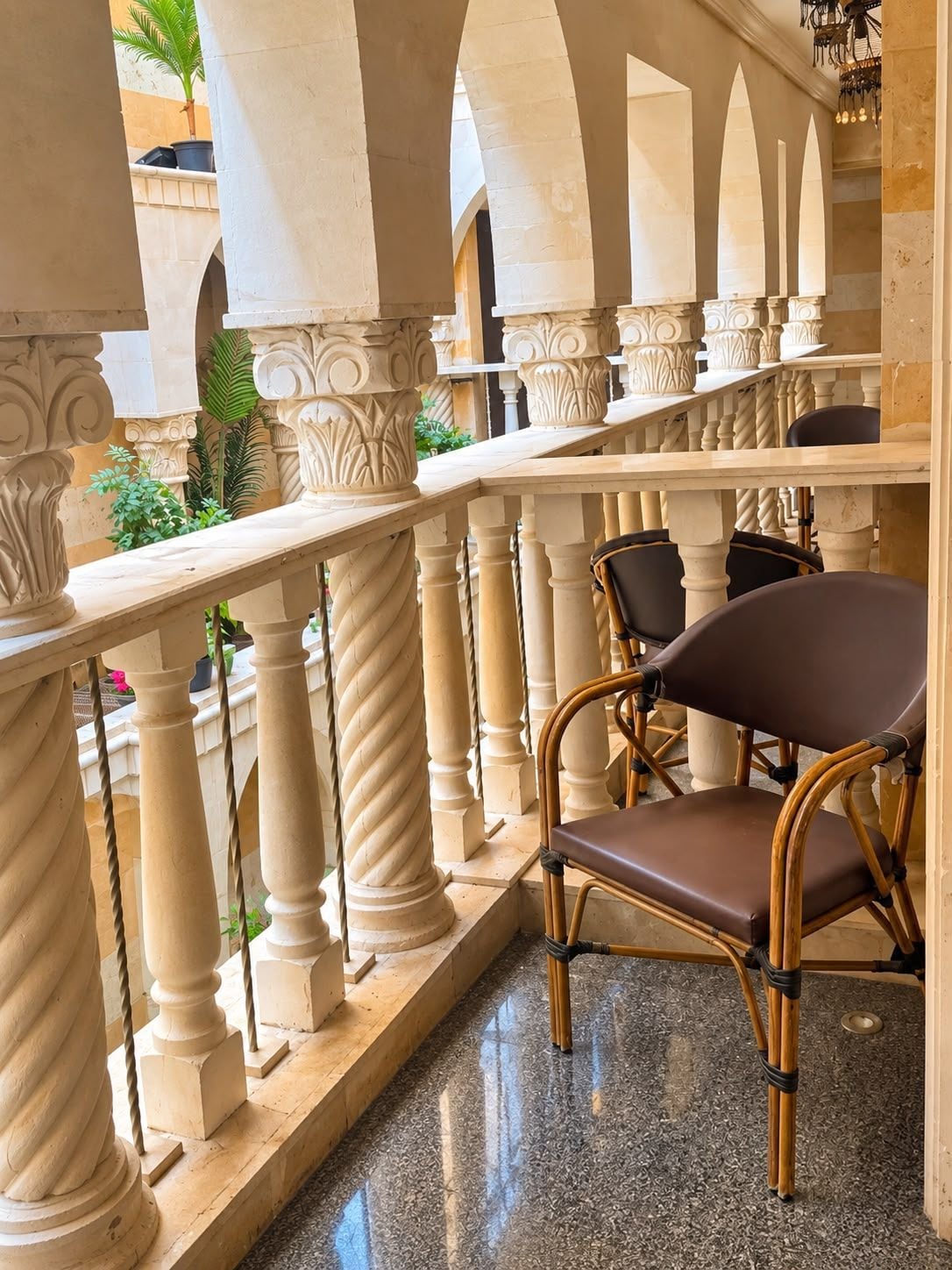 Un balcón con barandilla de hierro forjado, una silla de mimbre y vistas al patio.