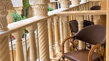 Un balcón con barandilla de hierro forjado, una silla de mimbre y vistas al patio.