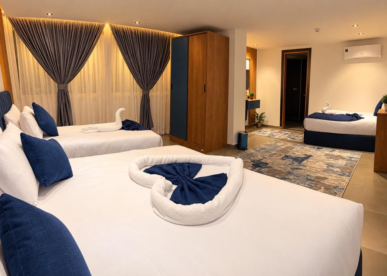 A hotel room with two beds, a wooden wardrobe, a bathroom, and a view of the city.