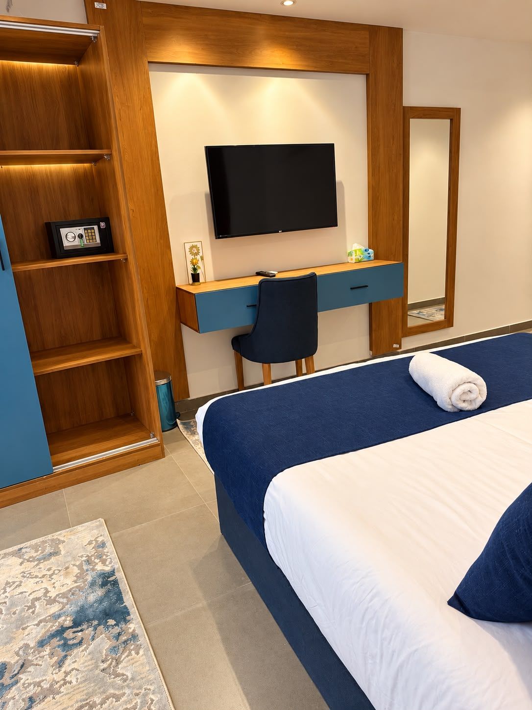 A hotel room with a bed, a desk with a chair, a television, a wardrobe, and a mirror.