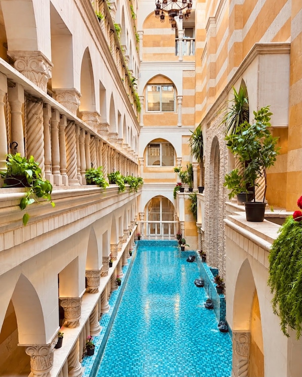 Una lujosa piscina interior con varios niveles de balcones, rodeada de arquitectura clásica y plantas en macetas.