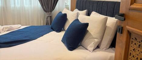 A hotel room with a bed, a nightstand, a wooden panel, and a window with curtains.