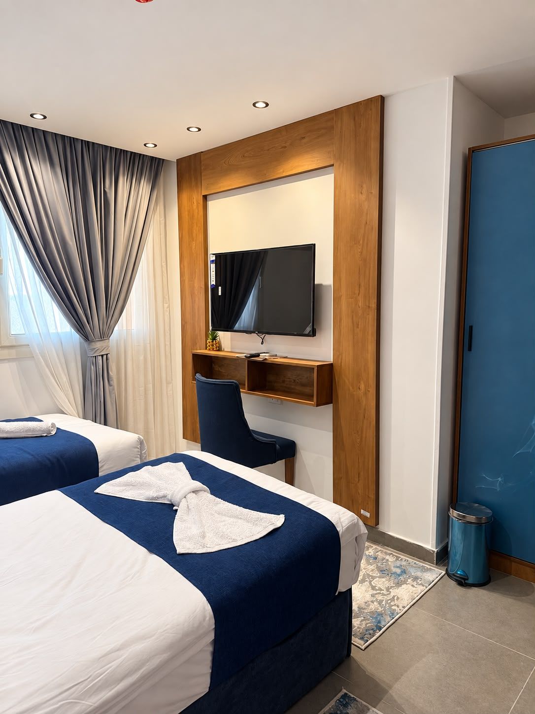 Ein Hotelzimmer mit zwei Betten, einem Schreibtisch, einem Fernseher und einer blauen Tür.