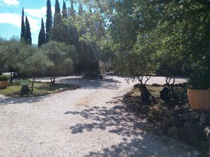 A gravel pathway leading to a building with a 'Welcome' sign, surrounded by trees and a stone wall. - COTTAGE LES OLIVIERS AT COTIGNAC (Cotignac)