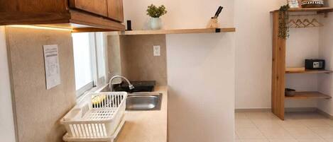 A kitchen with wooden cabinets, a white countertop, a sink, a small plant, and a hanging plant on a shelf.