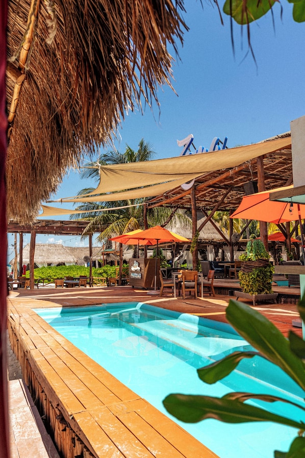 A pool area with wooden deck, umbrellas, and thatched roof structures.