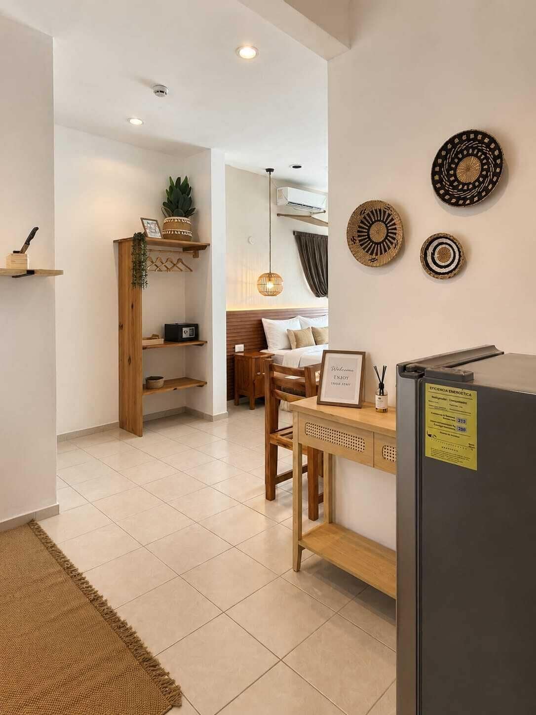 Una habitación moderna y bien iluminada con un escritorio de madera, una cama y una pequeña zona de kitchenette.
