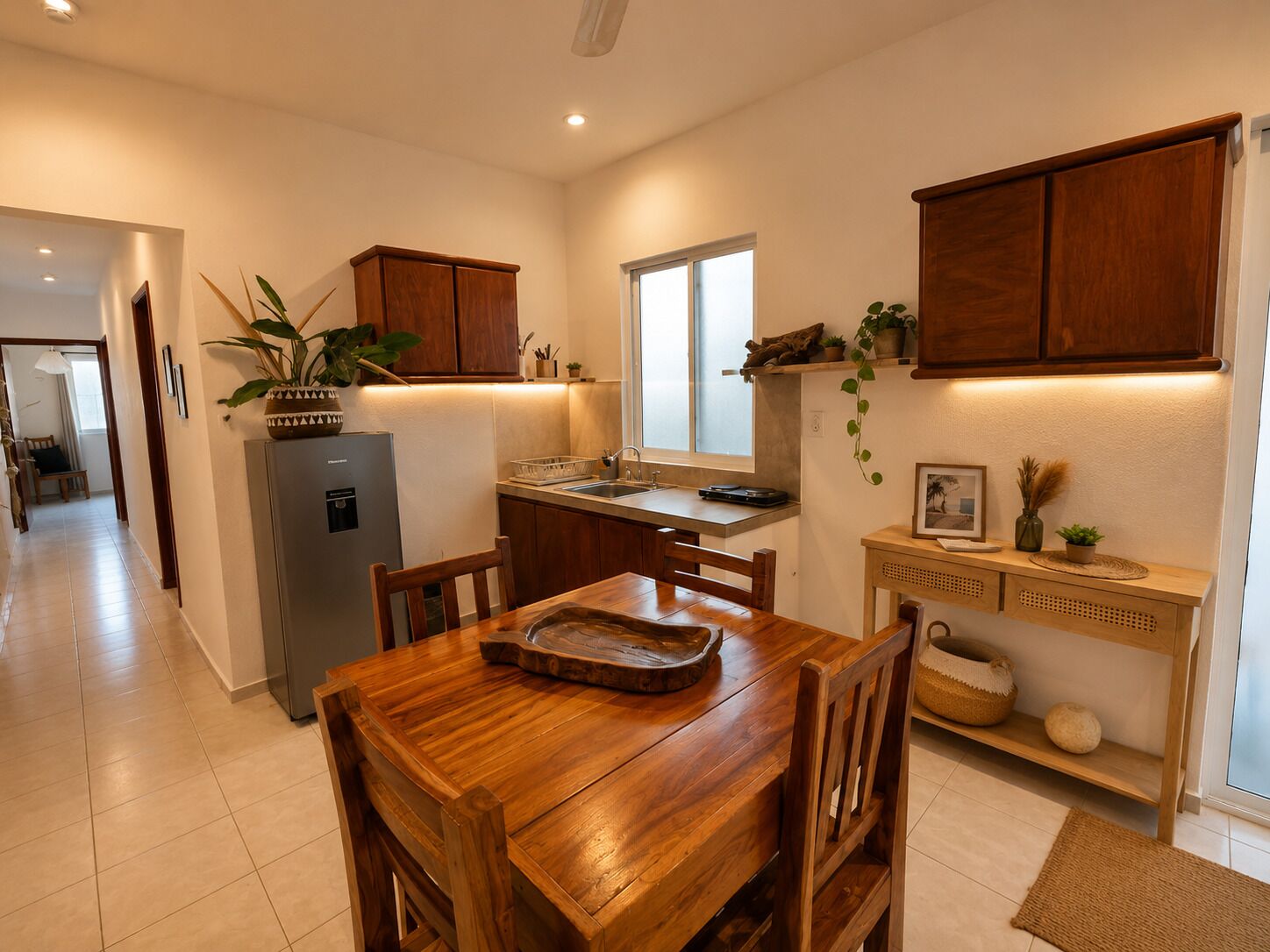 A compact kitchen with wooden cabinets, a refrigerator, a dining table with chairs, and a small island with a sink.