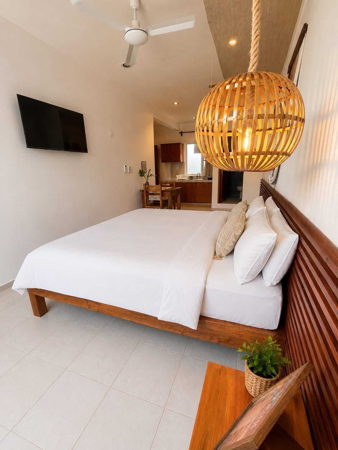 A bedroom with a bed, a TV, a ceiling fan, and a hanging light fixture.