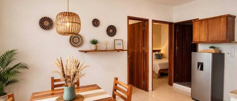 A dining area with a wooden table and chairs, a ceiling fan, and a kitchen with wooden cabinets and a refrigerator.