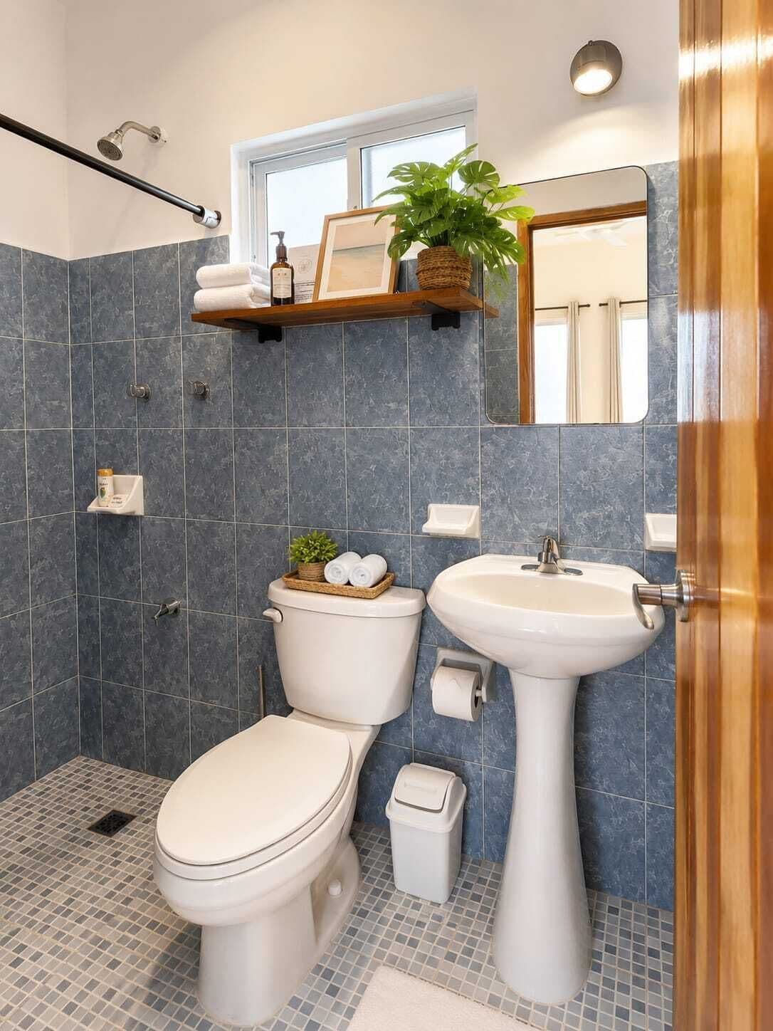 A bathroom with a toilet, sink, shower, and a window.