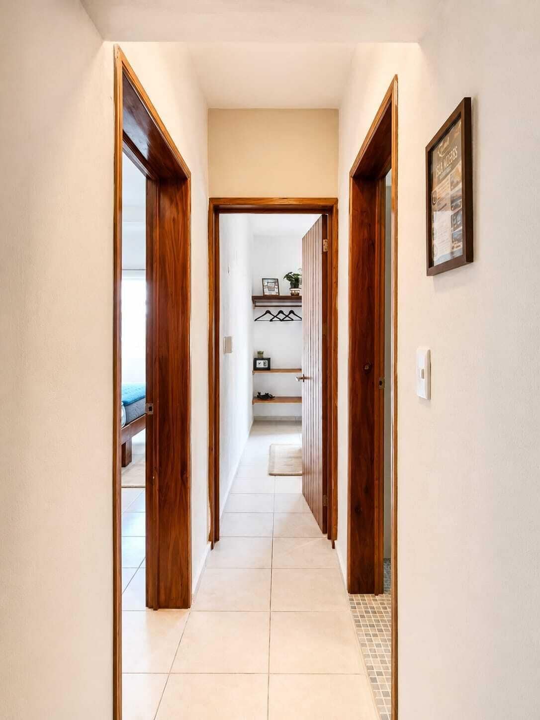 A hallway with wooden doors, a tiled floor, and a framed picture on the wall.