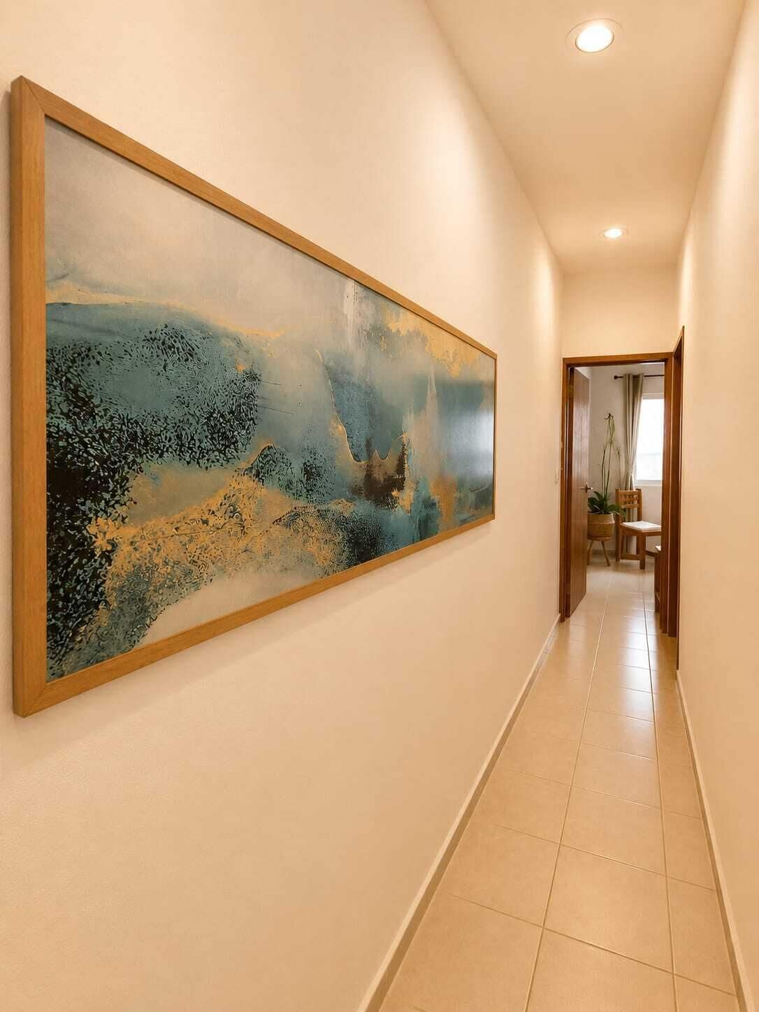 A hallway with a large abstract painting on the wall, a door at the end, and a tiled floor.