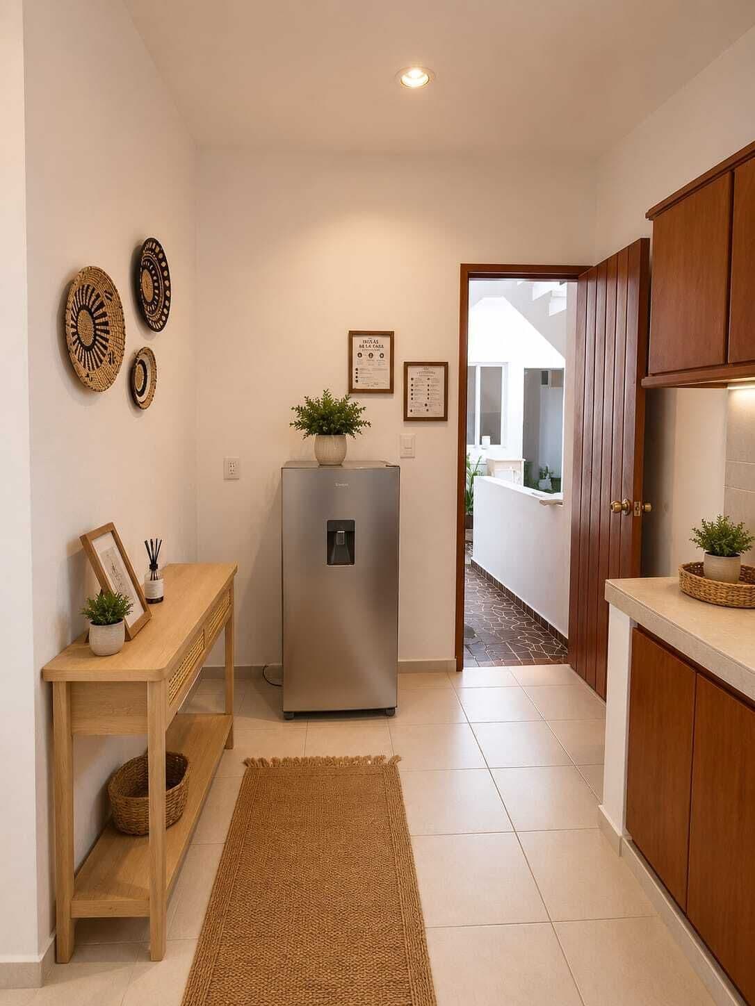 Una cocina compacta con refrigerador, gabinetes de madera, una mesita con una planta y platos decorativos en la pared.
