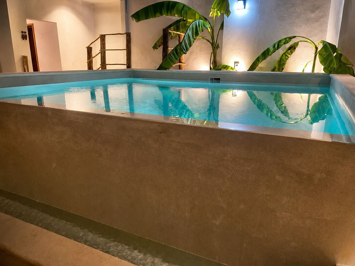 Una piscina interior con agua cristalina, rodeada de paredes y una escalera de madera.