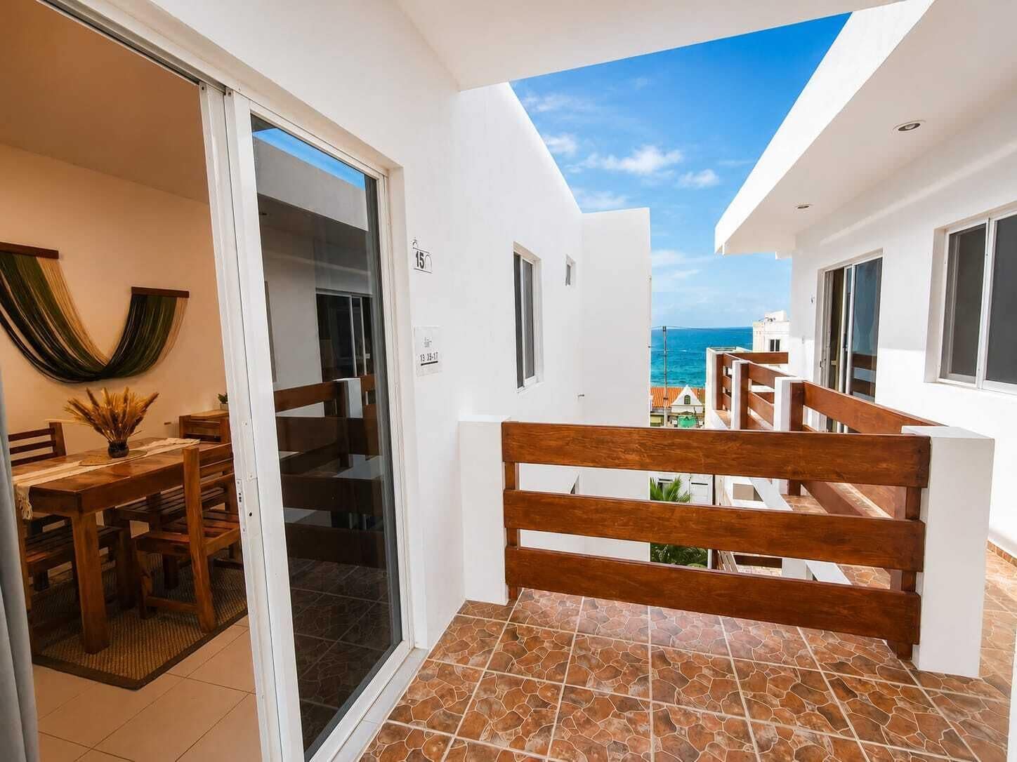 A balcony with a view of the sea, a dining area with a table and chairs, and a sliding glass door leading to a room.