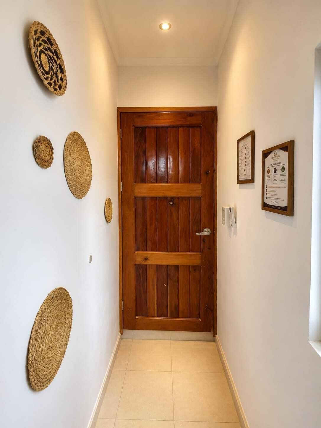 Un pasillo con puerta de madera, suelo de baldosas y varias decoraciones de pared tejidas.