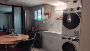 A compact kitchen with a washing machine, a dining table with chairs, and a refrigerator. - Our apartment welcomes you. Comfort and serenity..... (Bouzais)