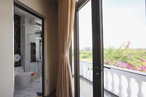 A balcony with a white balustrade, a view of greenery and flowers, and a bathroom with a marble floor and a toilet.