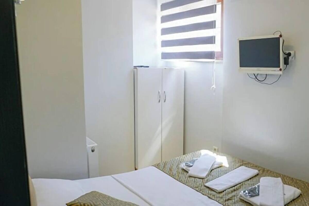 Habitación de hotel con cama, una mesita con silla, armario y televisor montado en la pared.