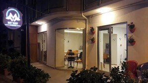 Entrada de hotel com porta de vidro, área de estar interna e plantas em vasos.