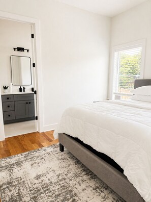Un dormitorio con cama, cómoda, espejo y ventana con vista a follaje.