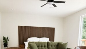 Una sala de estar moderna con un sofá verde, dos sillones marrones, un ventilador de techo y suelo de madera.