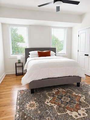 A bedroom with a bed, a ceiling fan, two windows, a door, and a patterned rug. - Spacious 4-bedroom house in tranquil Atlanta with AC (Atlanta)