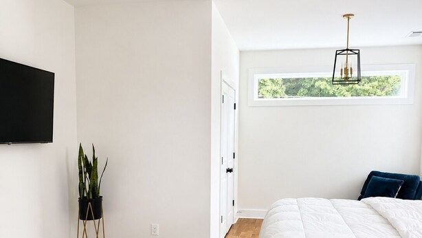 Un dormitorio con cama, ventilador de techo, televisor, planta y ventana con vista.