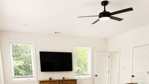 Un dormitorio con cama, sofá, aparador de madera, televisor y ventilador de techo.