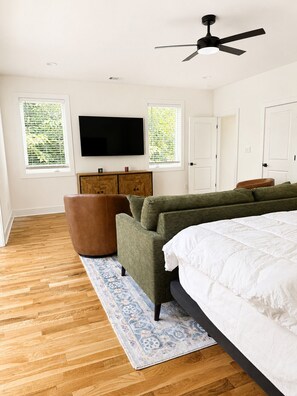 A bedroom with a bed, a sofa, a wooden cabinet, a television, and a ceiling fan.