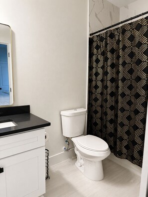 A bathroom with a white toilet, a black countertop, and a patterned shower curtain.