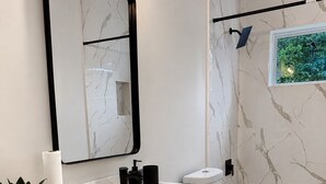 Un baño moderno con tocador de mármol, un espejo grande, inodoro y bañera.