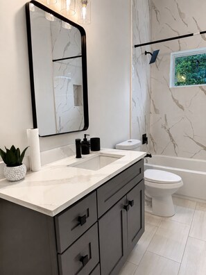 A modern bathroom with a marble vanity, a large mirror, a toilet, and a bathtub.