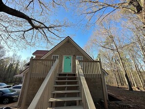 Eine Holzhütte mit grüner Tür und einer Treppe, die zum Eingang führt, vor dem Hintergrund eines Waldes.