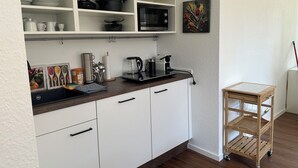 A kitchen with white cabinets, a microwave, a coffee maker, and a small wooden cart. - Sechser in Münster Roxel—10 minutes from the UKM (Münster)