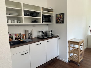 A kitchen with white cabinets, a microwave, a coffee maker, and a small wooden cart. - Sechser in Münster Roxel—10 minutes from the UKM (Münster)