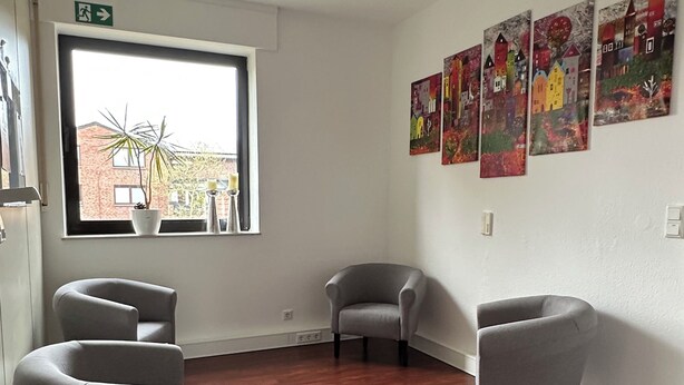 A room with a wooden floor, two grey armchairs, a window with a view of buildings, and three colorful paintings on the wall. - Sechser in Münster Roxel—10 minutes from the UKM (Münster)