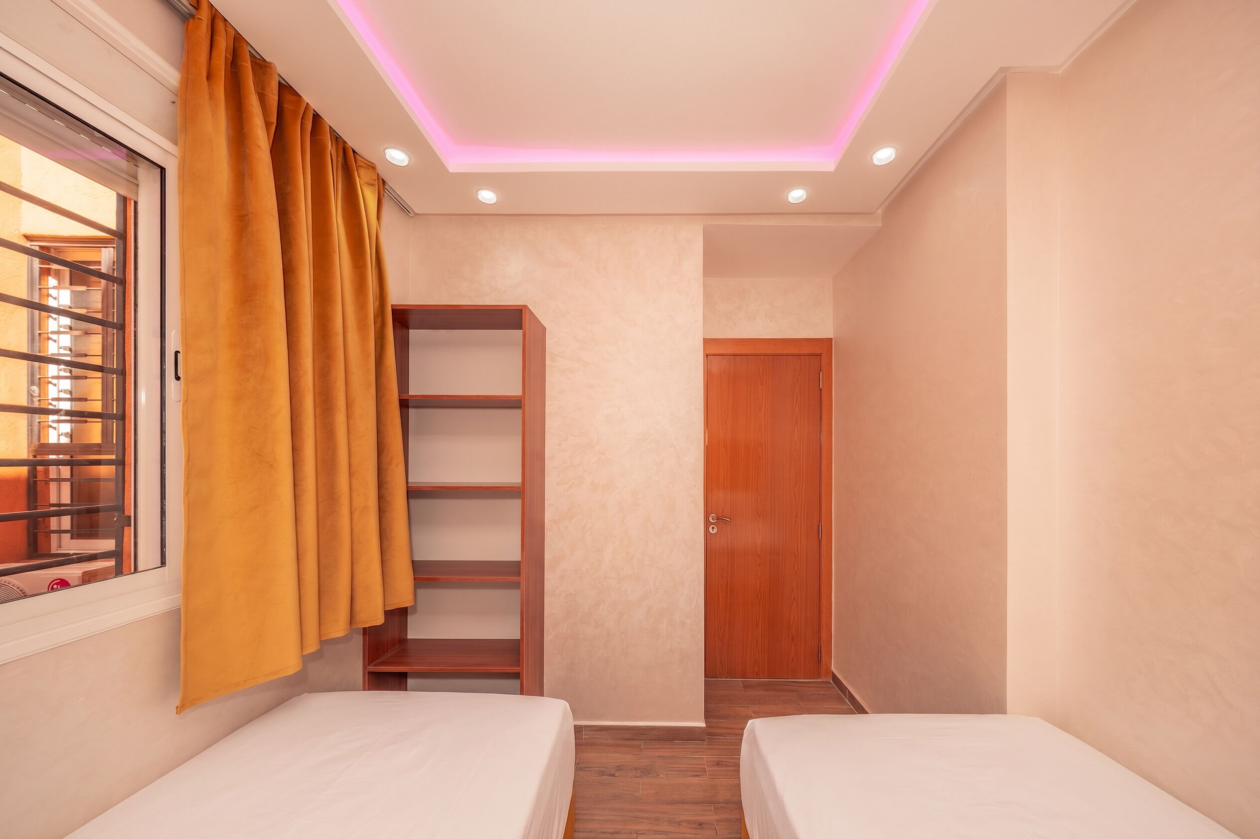 A room with two beds, a wooden wardrobe, a shelf unit, and a window with curtains.