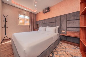 A modern hotel room with a large bed, a headboard with storage, a coat rack, and a window with curtains. - Chic New Appartement Steps from Shops and Restaurants  —Your Perfect Urban Retreat (Marrakech)