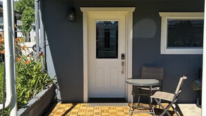 Een overdekt terras met een houten vloer, een witte deur en een kleine tafel met stoelen.