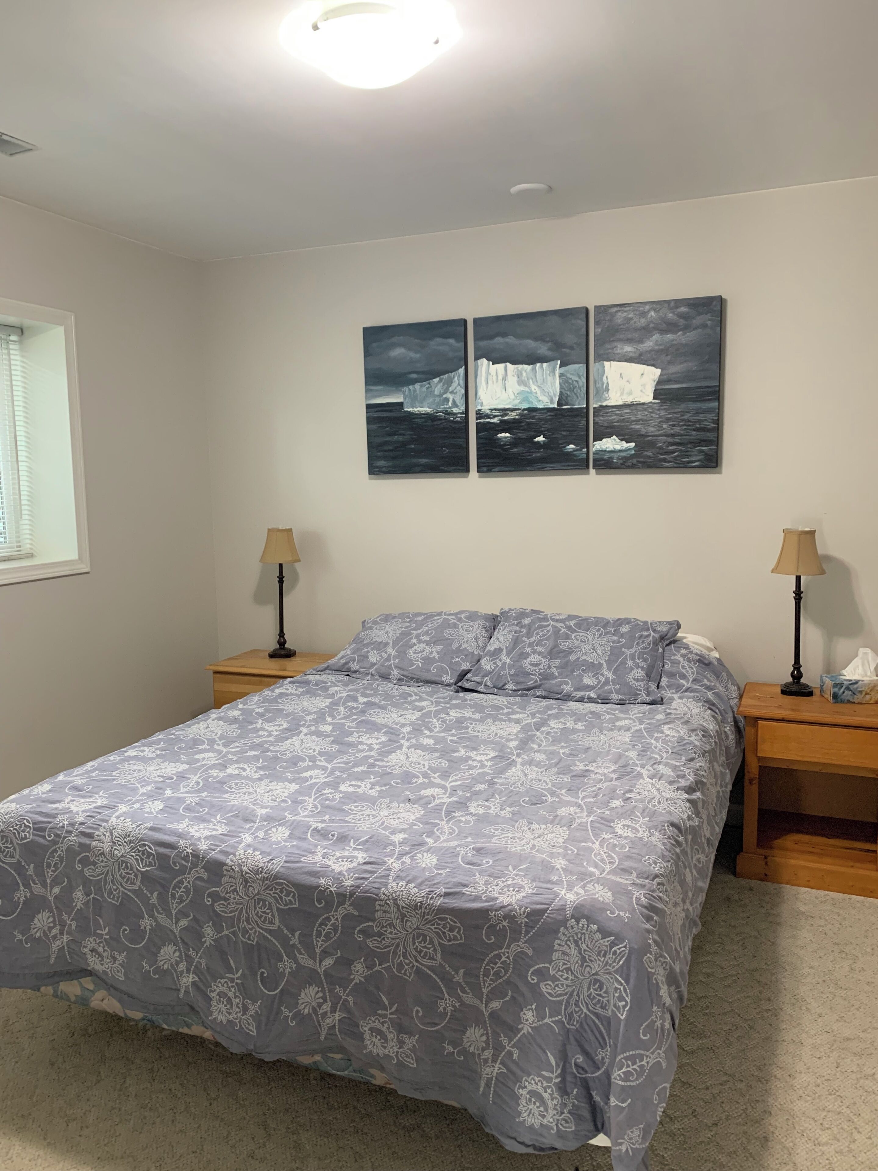 Une chambre à coucher comprenant un lit, deux tables de chevet, une fenêtre et deux tableaux accrochés au mur.