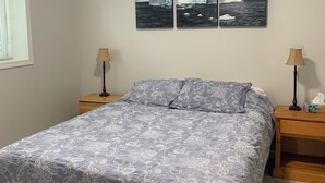 Een slaapkamer met een bed, twee nachtkastjes, een raam en twee aan de muur hangende schilderijen.