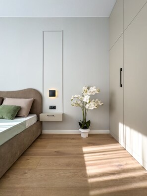 Une chambre à coucher moderne avec un lit, une table de chevet, une lampe de chevet, un luminaire fixé au mur et une orchidée en pot.
