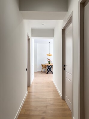 Ein Flur mit Holzboden, weißen Wänden und Türen zu einem Zimmer mit Tisch und Stuhl.