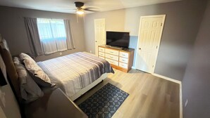 A bedroom with a bed, a TV on a wooden dresser, a ceiling fan, and a window with curtains. - Private 3BR Pool Retreat Near Houston (Deer Park)
