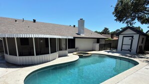 A swimming pool with a curved edge, a covered patio area, and a house with a chimney. - Private 3BR Pool Retreat Near Houston (Deer Park)