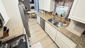 Uma cozinha compacta com armários brancos, bancada de granito, pia e um espaço de refeições com mesa e cadeiras.