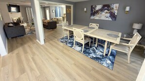 Uma sala de estar moderna com área de jantar, piso de madeira e um grande quadro abstrato na parede.